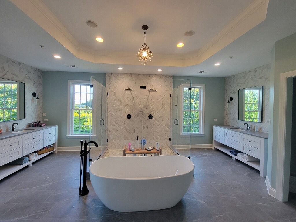 Opulent bathroom remodel by Bupp Contracting LLC featuring a spacious freestanding tub, dual showers, and elegant dual vanities set against a large window.